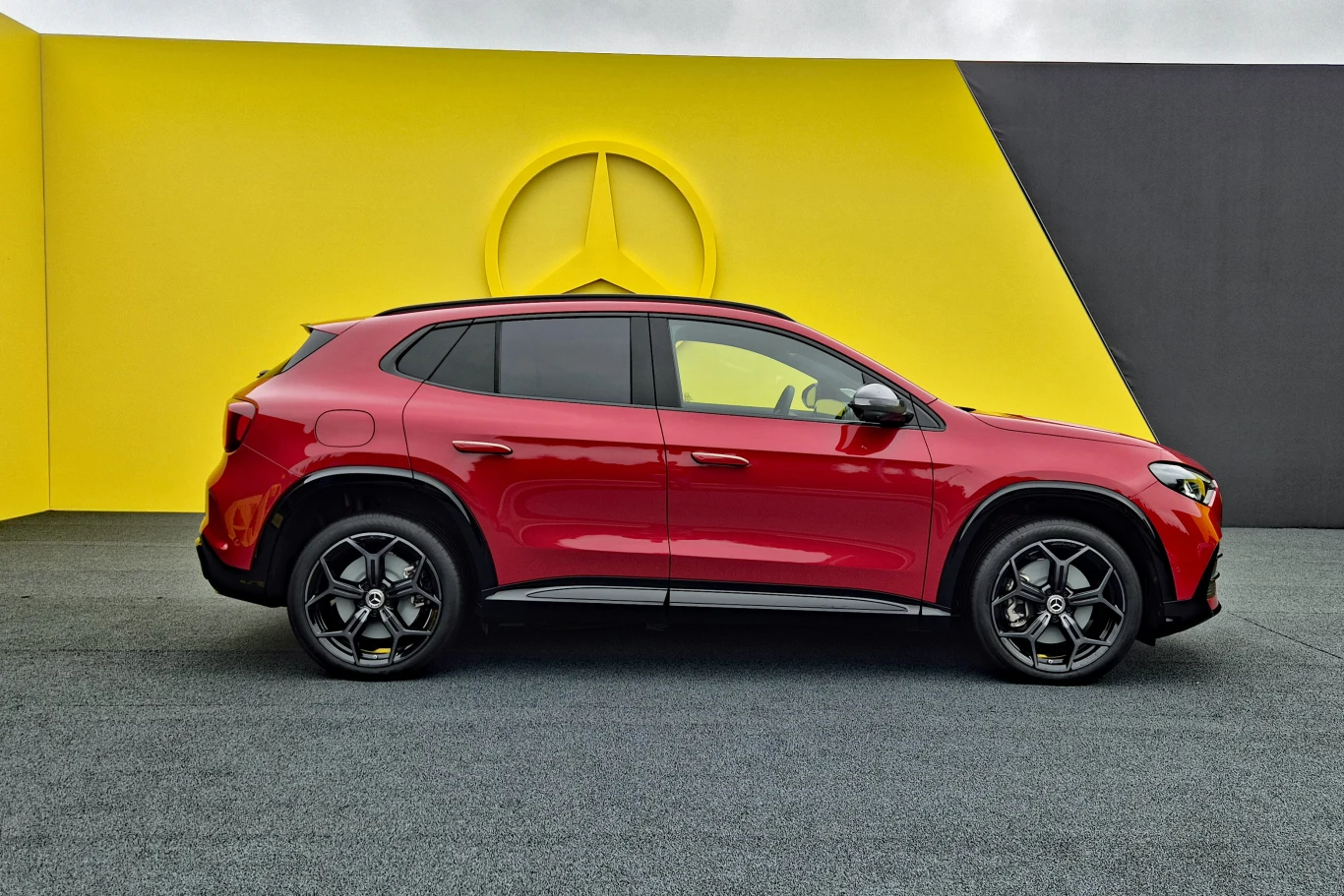Czerwony SUV Mercedes-Benz ustawiony bokiem na tle żółto-czarnej ściany z dużym logo marki.