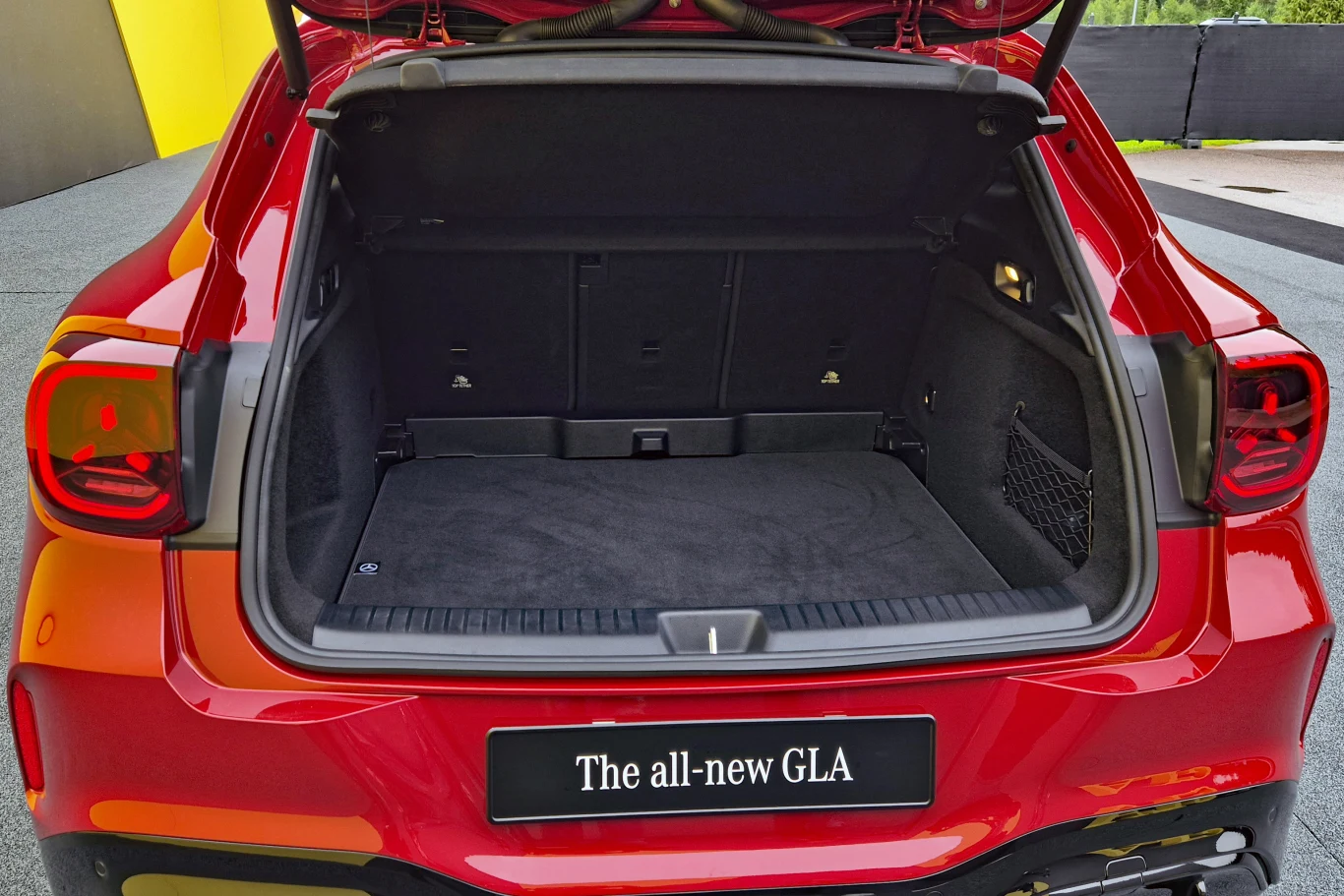 Czerwony samochód typu SUV z otwartą przestronną bagażnikiem, na tylnym zderzaku widoczna czarna tablica z napisem „The all-new GLA”.