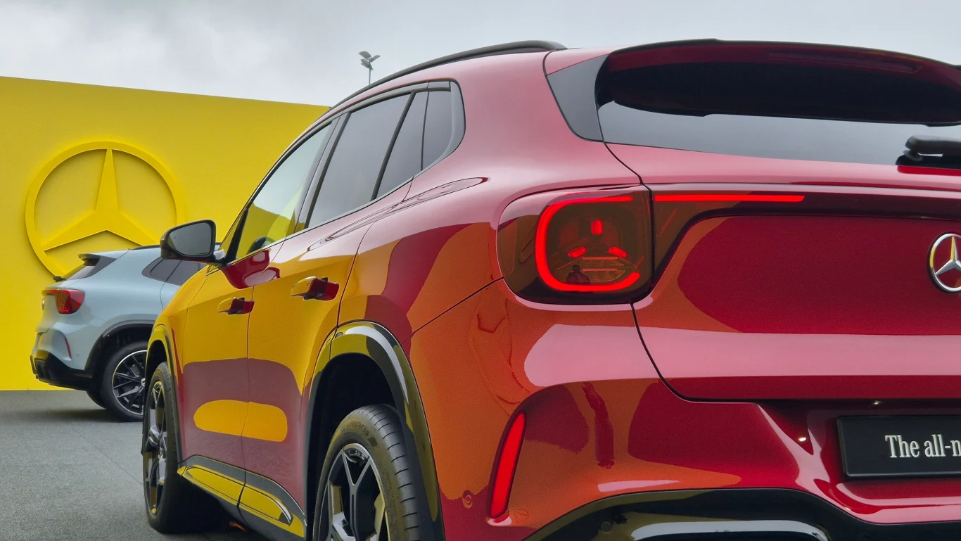 Dwa nowoczesne SUV-y marki Mercedes-Benz zaparkowane obok siebie, na tle żółtej ściany z dużym logo producenta.
