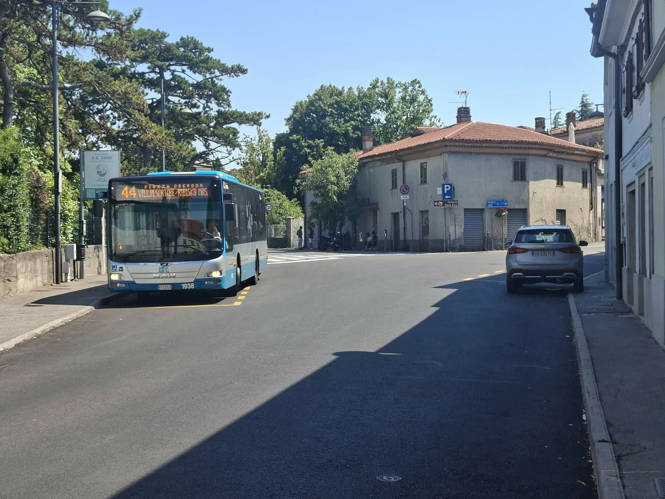 Autobus komunikacji miejskiej linii 44 jedzie ulicą wśród budynków, po prawej stronie zaparkowany samochód osobowy.
