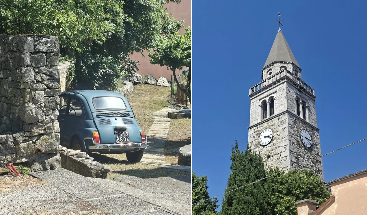 Mały niebieski samochód osobowy zaparkowany przy kamiennym murze oraz wysoka, kamienna wieża kościelna z zegarem i krzyżem na szczycie, otoczona zielenią.