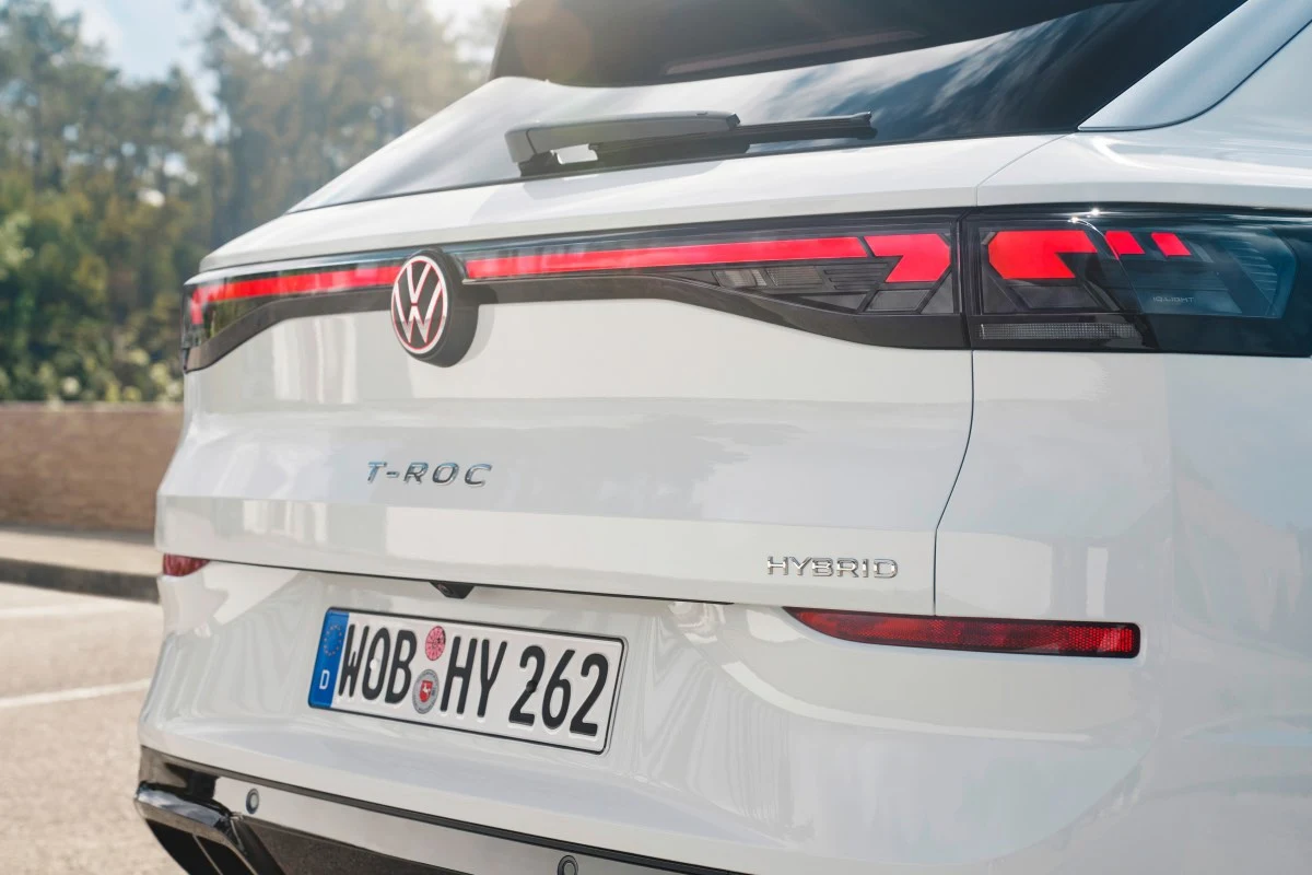 Tylny fragment białego samochodu Volkswagen T-Roc Hybrid z wyraźnymi lampami LED, emblematem marki oraz niemiecką tablicą rejestracyjną.