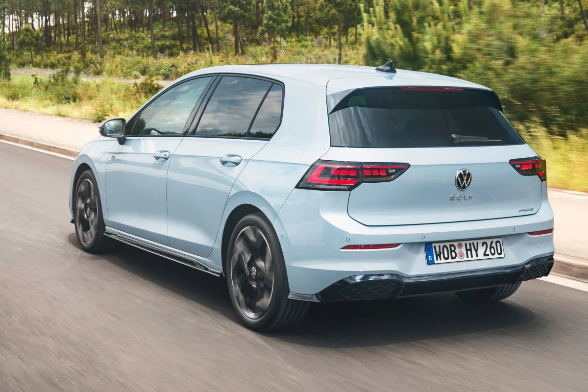 Jasnoniebieski Volkswagen Golf z przyciemnianymi szybami i czarnymi felgami w ruchu na asfaltowej drodze, otoczonej zielenią.