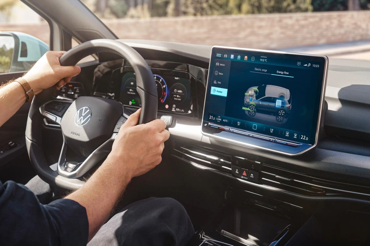 Kierownica samochodu marki Volkswagen trzymana przez osobę, cyfrowy kokpit i duży ekran dotykowy systemu multimedialnego prezentujący wizualizację pojazdu oraz dane dotyczące jazdy.