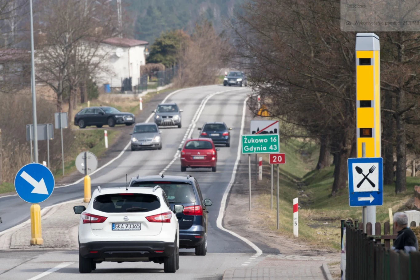 Kilka samochodów poruszających się dwupasmową, krętą drogą wyposażoną w fotoradar oraz drogowskaz wskazujący kierunki do Żukowa i Gdyni.