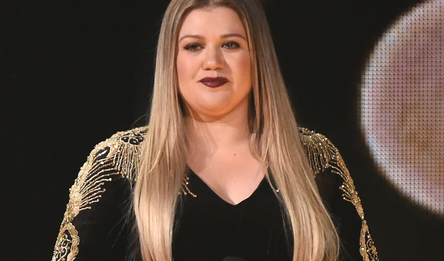 Kelly Clarkson Kelly Clarkson w czarnej kreacji ze złotymi zdobieniami na ramionach podczas występu na scenie.