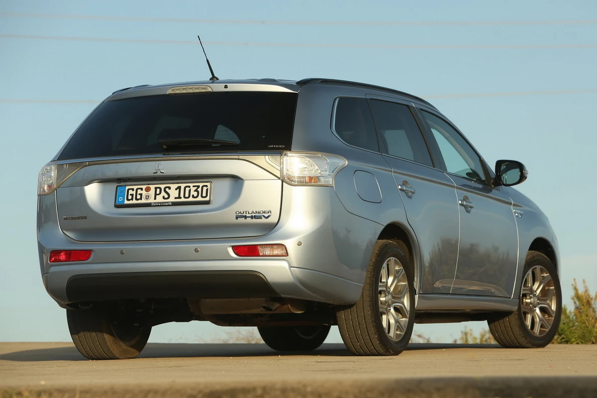 Srebrny SUV Mitsubishi Outlander Plug-In Hybrid stoi na płaskiej nawierzchni, widoczny z tyłu i z boku, z wyraźnie widoczną tablicą rejestracyjną oraz detalami tylnych lamp.