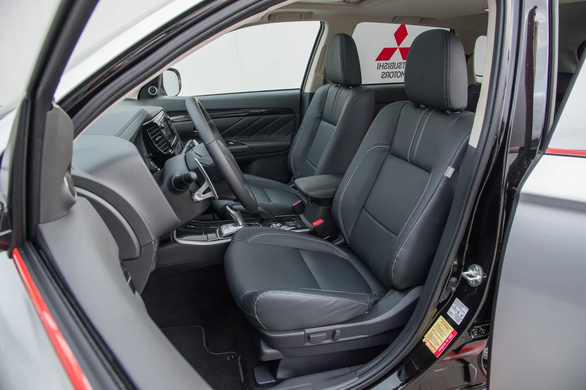Kokpit samochodu ze skórzanymi fotelami, nowoczesną deską rozdzielczą i wielofunkcyjną kierownicą, widoczne logo Mitsubishi na zagłówku pasażera z tyłu.