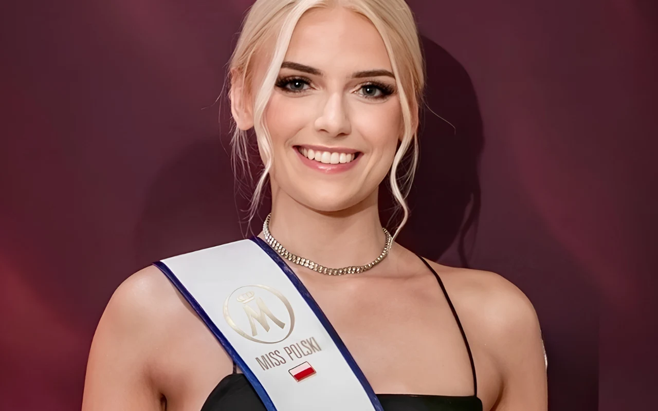 Uśmiechnięta kobieta o jasnych włosach w eleganckiej czarnej sukni, nosząca szarfę z napisem „Miss Polski” ozdobioną flagą Polski, stoi na bordowym tle.