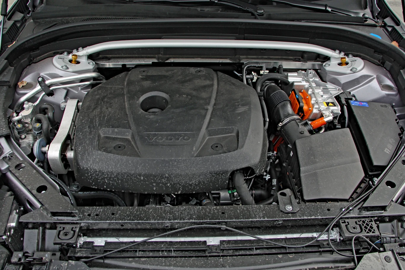 Komora silnika samochodu Volvo z widoczną jednostką napędową przykrytą czarną osłoną, po prawej stronie elementy układu elektrycznego z pomarańczowymi przewodami.