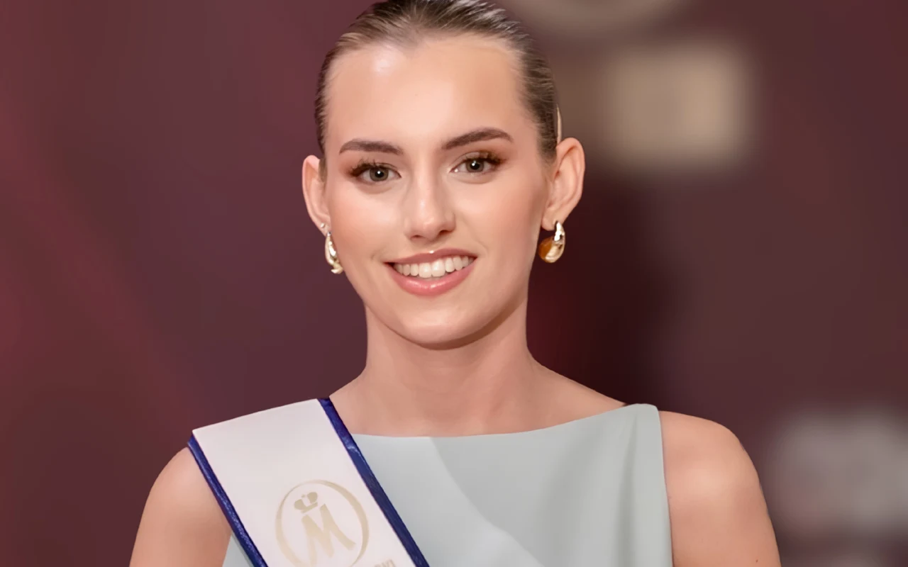 Uśmiechnięta młoda kobieta z upiętymi włosami, ubrana w elegancką sukienkę i szarfę, ozdobiona subtelną biżuterią, pozuje na tle w efektownym świetle.