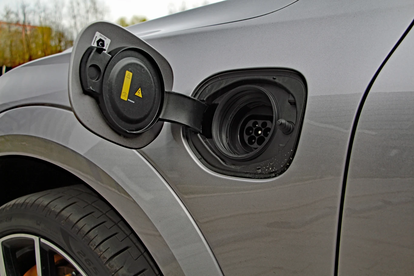 Gniazdo ładowania samochodu elektrycznego z otwartą klapką na błotniku szarego pojazdu.