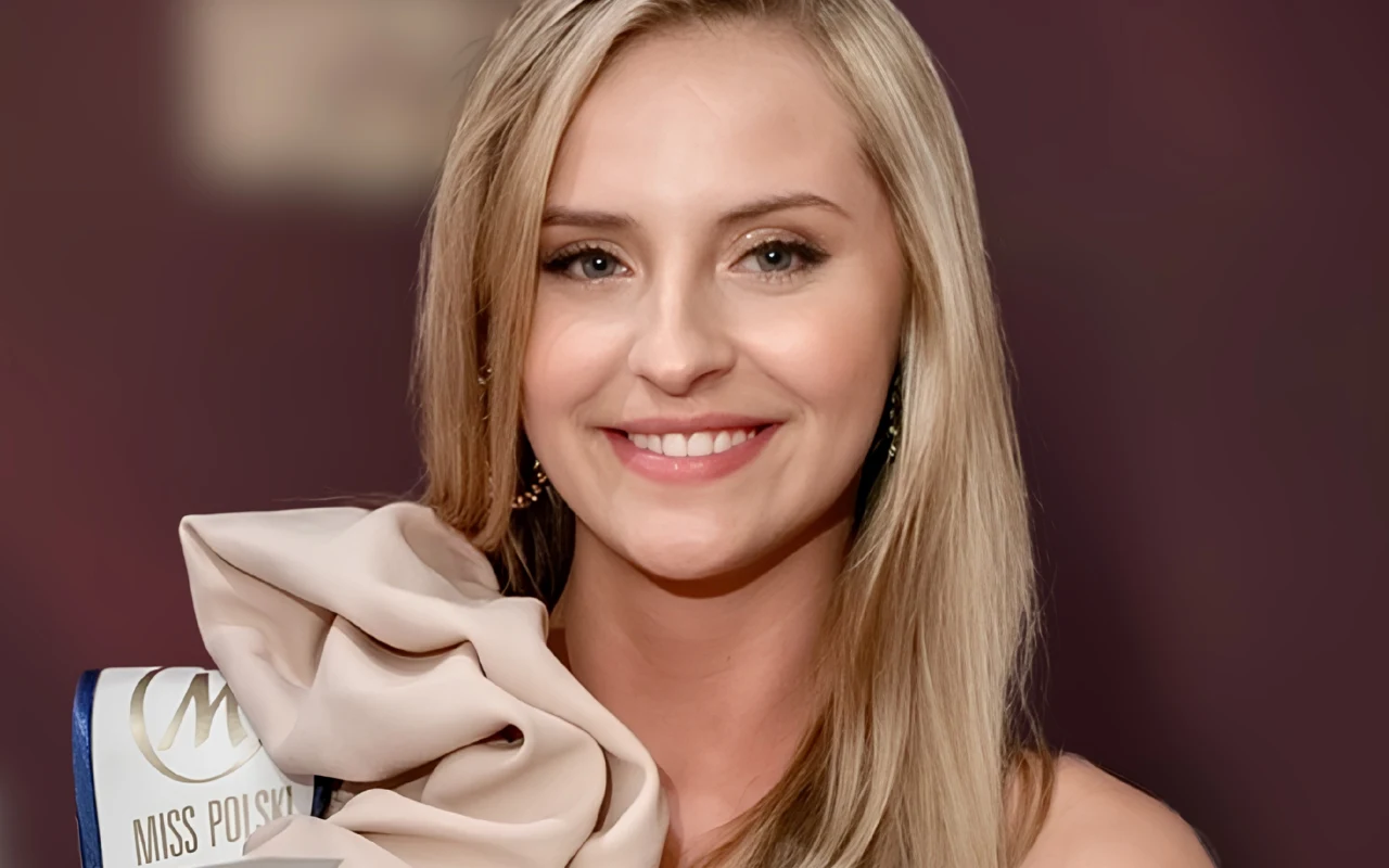 Uśmiechnięta kobieta z długimi blond włosami, ubrana elegancko, z szarfą z napisem „Miss Polski” przewieszoną przez ramię.
