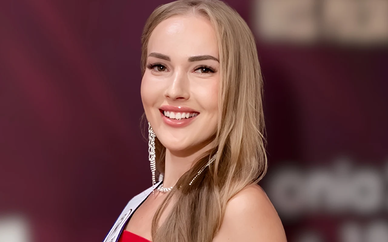 Uśmiechnięta młoda kobieta z długimi blond włosami, ubrana w elegancką czerwoną suknię i długie, lśniące kolczyki.