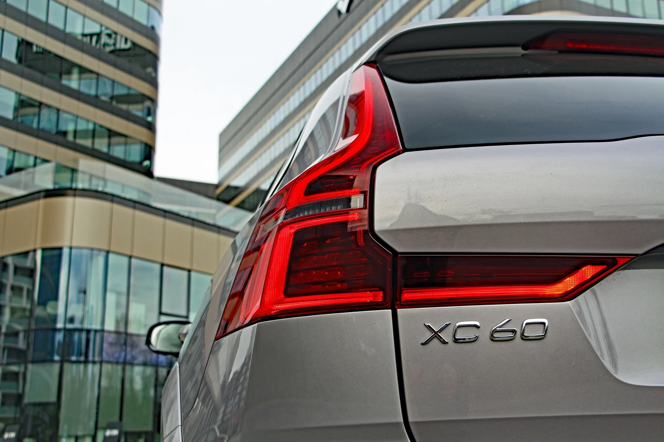 Srebrny SUV Volvo XC60 z charakterystycznym tylnym światłem LED, zaparkowany przy nowoczesnych szklanych biurowcach.