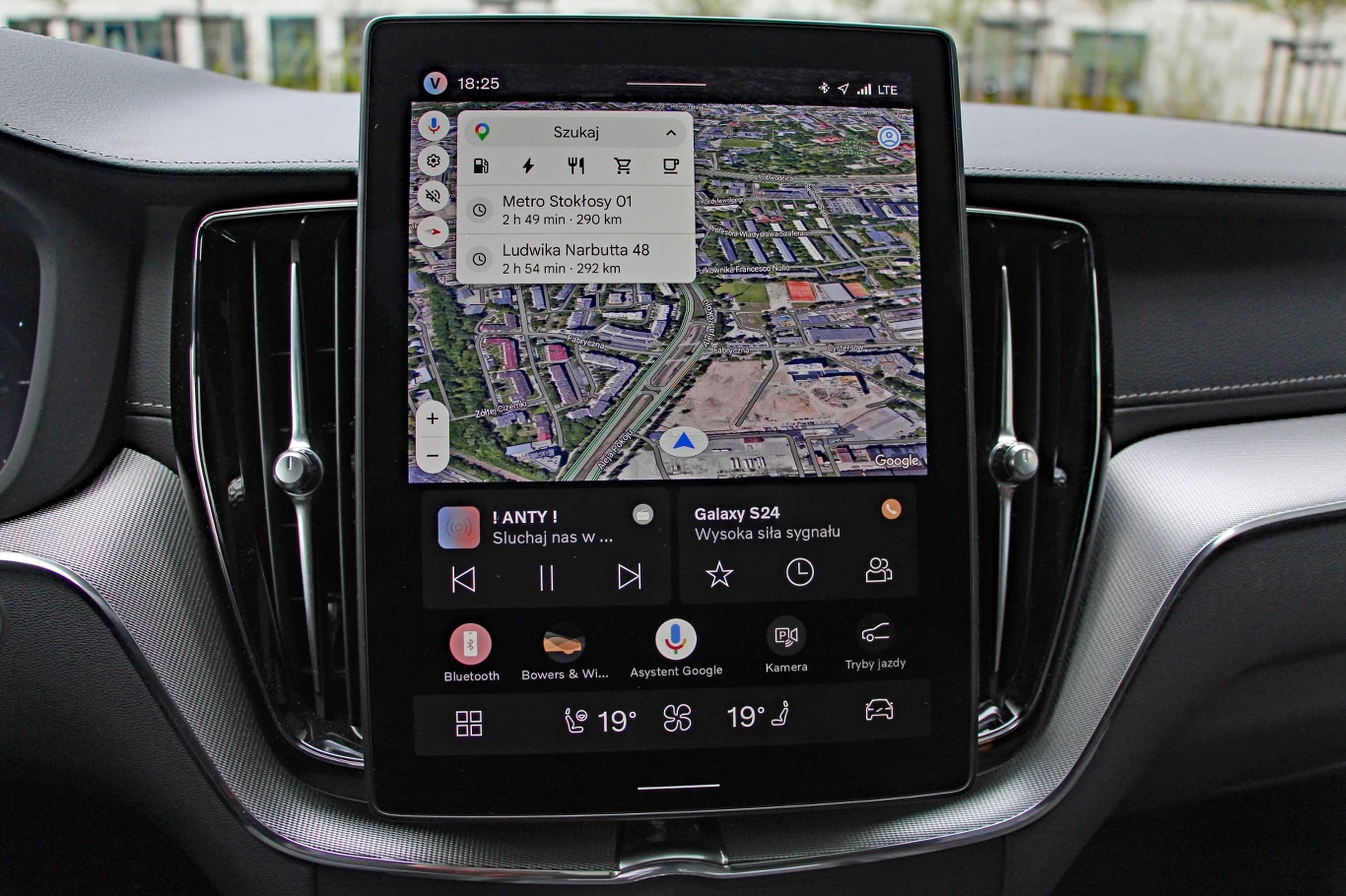 Duży ekran dotykowy samochodowego systemu multimedialnego z uruchomioną nawigacją Google Maps oraz widocznymi ikonami sterowania radiem, klimatyzacją i funkcjami pojazdu.