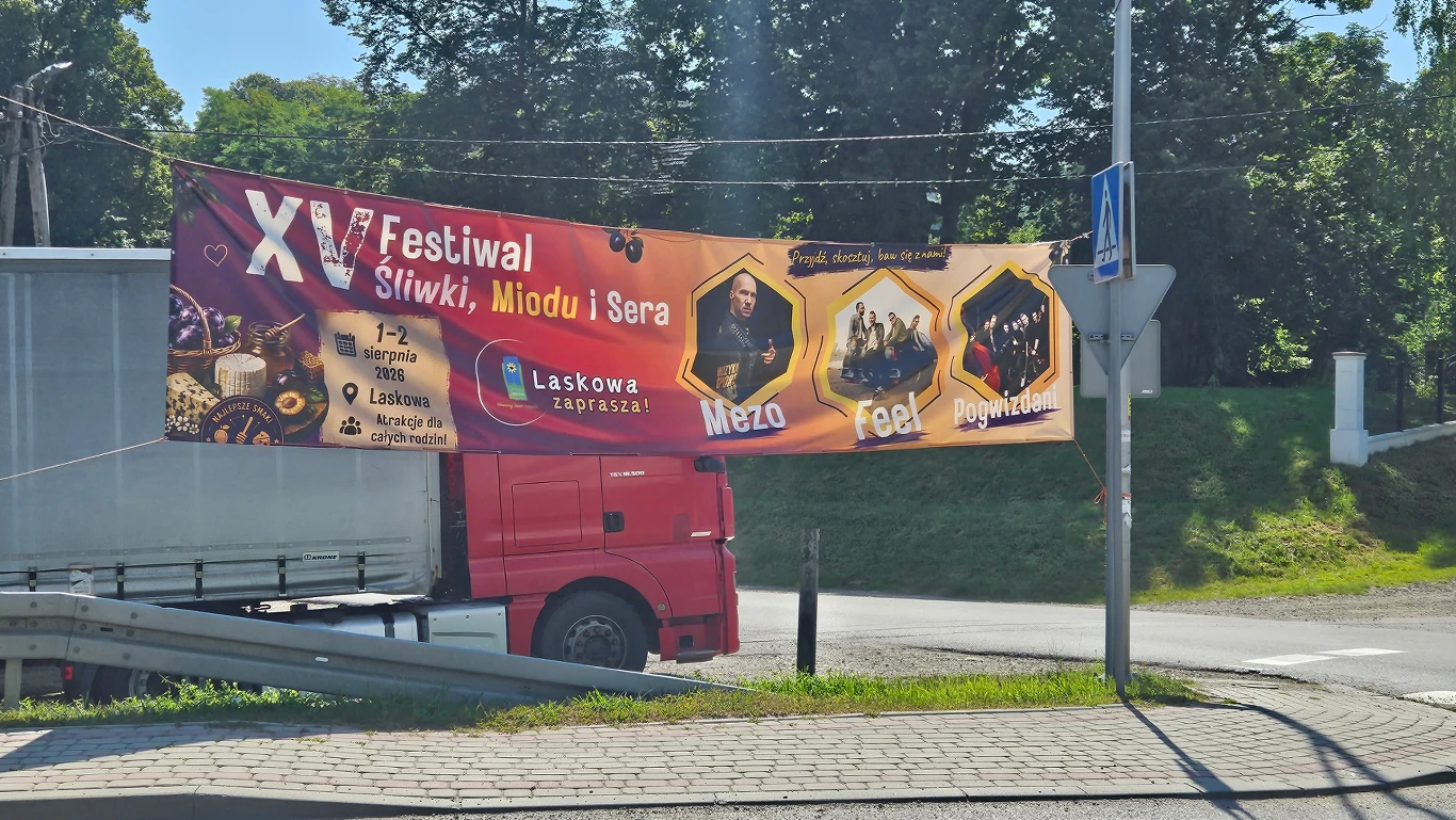 Baner reklamujący festiwal Baner reklamowy XV Festiwalu Śliwki, Miodu i Sera z informacją o terminie i miejscu wydarzenia, nazwami zespołów muzycznych oraz kolorową grafiką na tle czerwonej ciężarówki i zieleni.