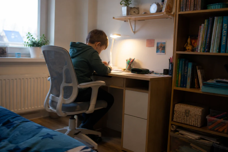 Kącik do nauki — biurko, krzesło i lampka w pokoju ucznia Kącik do nauki w pokoju dziecka — biurko przy oknie, lampka LED, krzesło obrotowe i regał z książkami