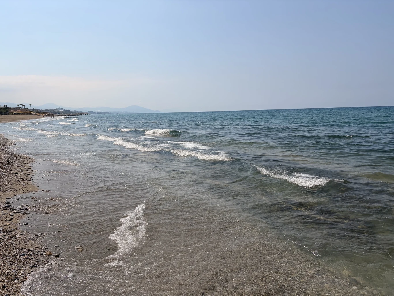 Jak widać obiecywana piaszczystość plaży znikała i zamieniała się w kamienistość przy samym morzu Piaszczysto-kamienista plaża z łagodnie falującym, błękitnym morzem i spokojną linią horyzontu.