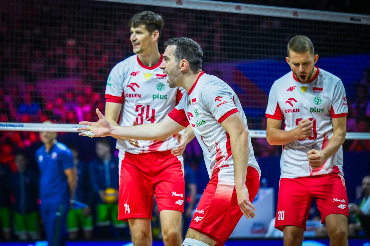 Siatkarze reprezentacji Polski Trzech siatkarzy w białych i czerwonych strojach z orzełkiem i logotypami sponsorów stoi blisko siatki na boisku, wyrażając emocje po akcji podczas meczu.