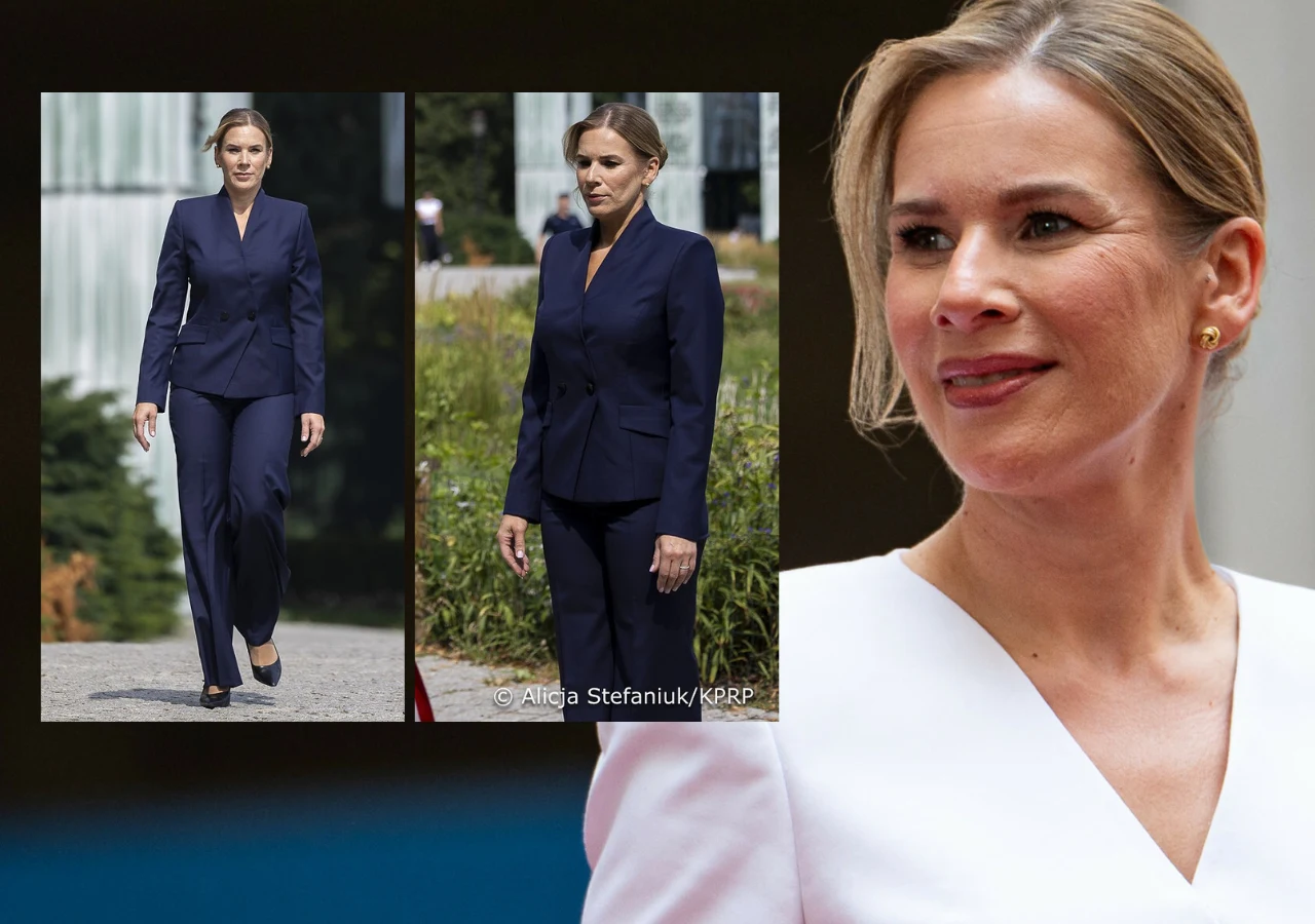 Marta Nawrocka Kobieta ubrana w granatowy garnitur z prostymi spodniami i zapinaną na jeden guzik marynarką, włosy zaczesane do tyłu w niskim koku, delikatny makijaż, elegancki, minimalistyczny styl.