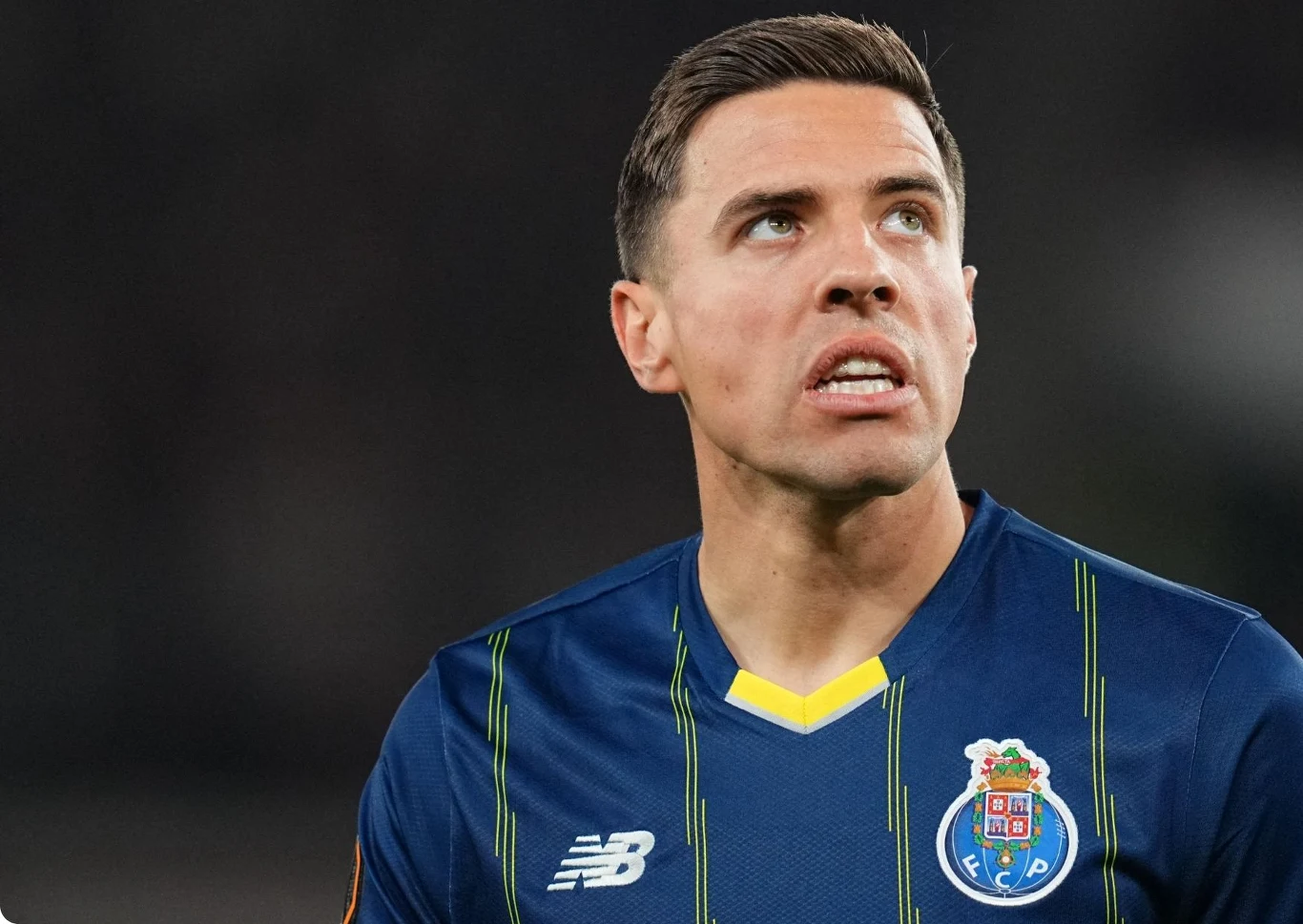 Piłkarz w granatowej koszulce z herbem klubu FC Porto i logo New Balance patrzący w górę.