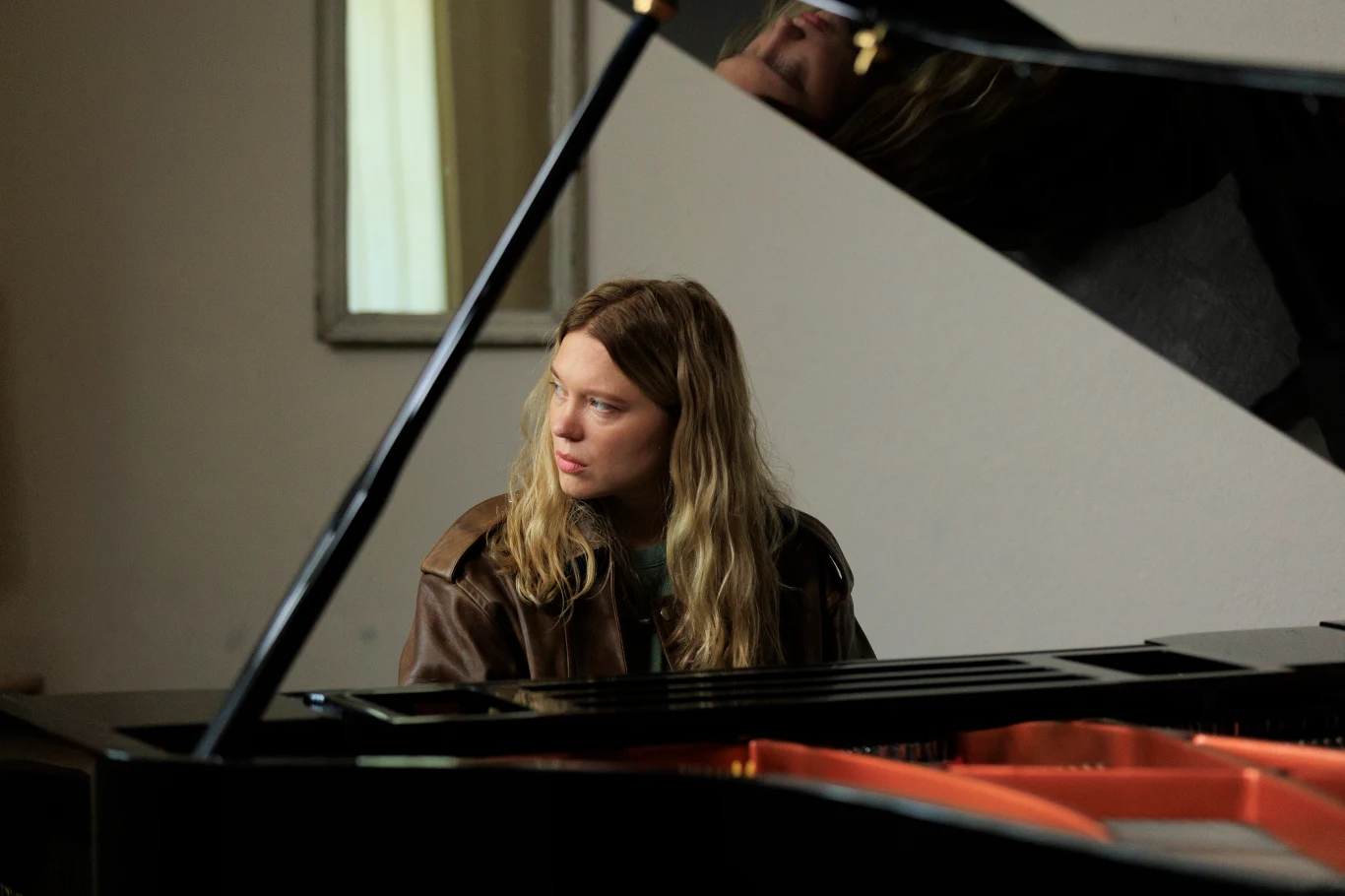 Kadr z filmu "Gentle Monster" Kobieta z długimi blond włosami siedzi przy fortepianie, spoglądając w bok w zamyśleniu.