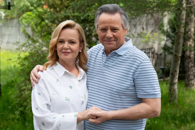 Para dojrzałych osób obejmuje się i trzyma za ręce, stojąc blisko siebie na tle zielonego ogrodu.