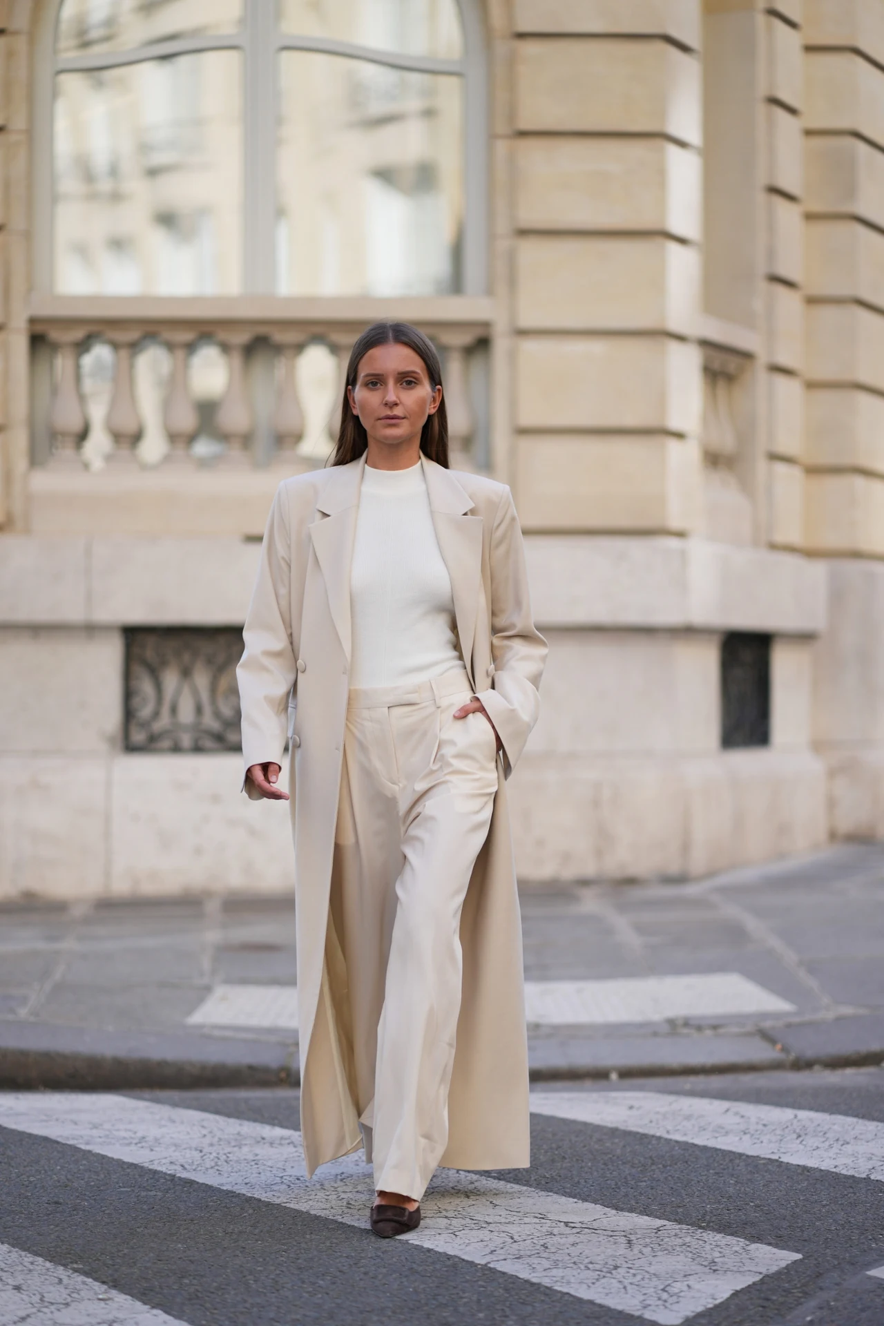 Biel i beż w eleganckim wydaniu. Diane Batoukina w minimalistycznej stylizacji Kobieta w eleganckim beżowym garniturze i białym golfie, idąca pewnym krokiem po pasach na tle miejskiej architektury.