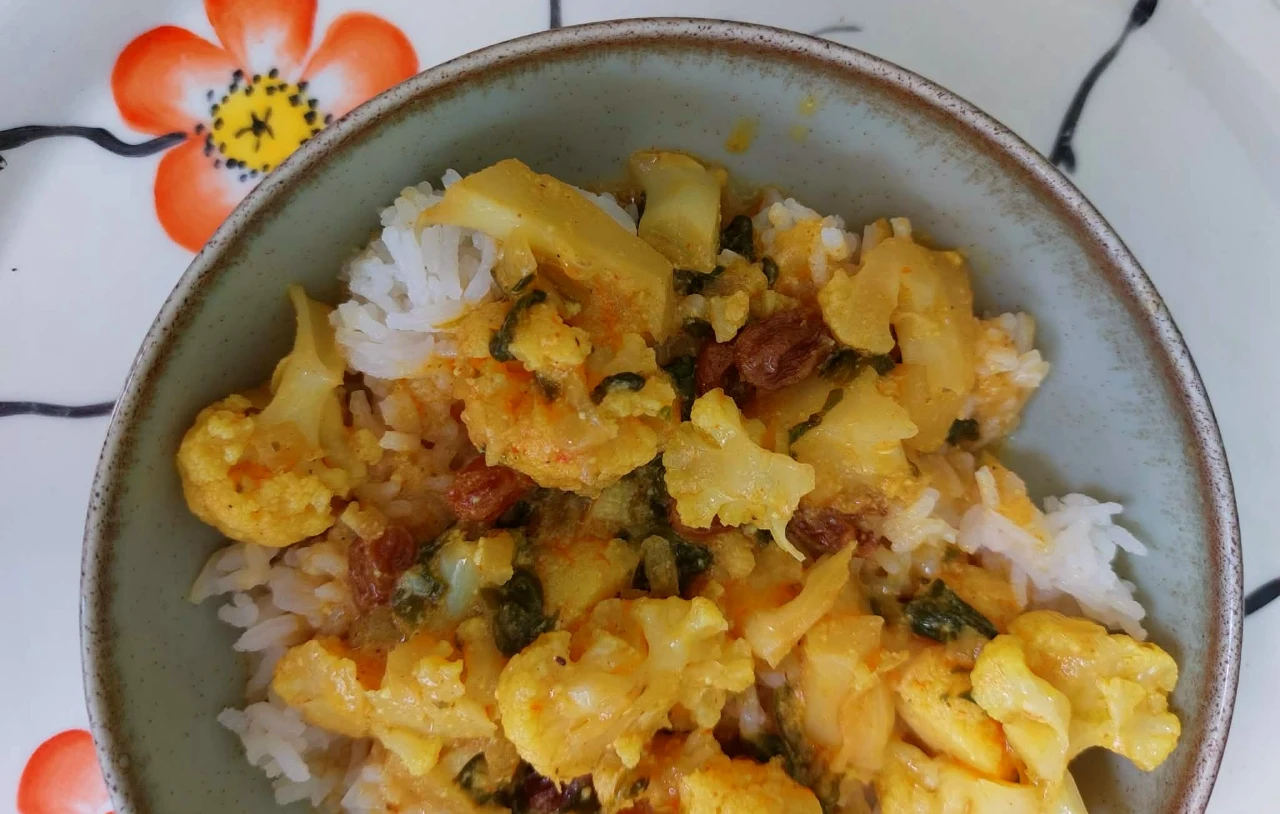 Kalafior w tej wersji dosłownie znika z talerzy. Wegańskie curry sprawdzi się, gdy masz dość mięsa Porcja wegańskiego curry z kalafiorem, rodzynkami i przyprawami, podana z ryżem w misce.