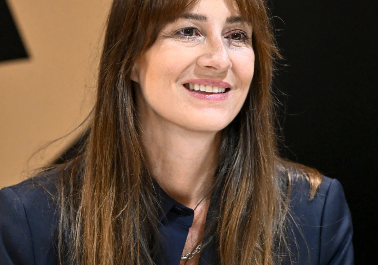 Maja Ostaszewska Maja Ostaszewska w granatowej marynarce siedząca przy stole.