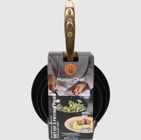 Zestaw trzech czarnych patelni z złotym uchwytem, zapakowanych w opakowanie z logo MasterChef, na którym widoczny jest talerz z daniem oraz osoba przygotowująca posiłek.