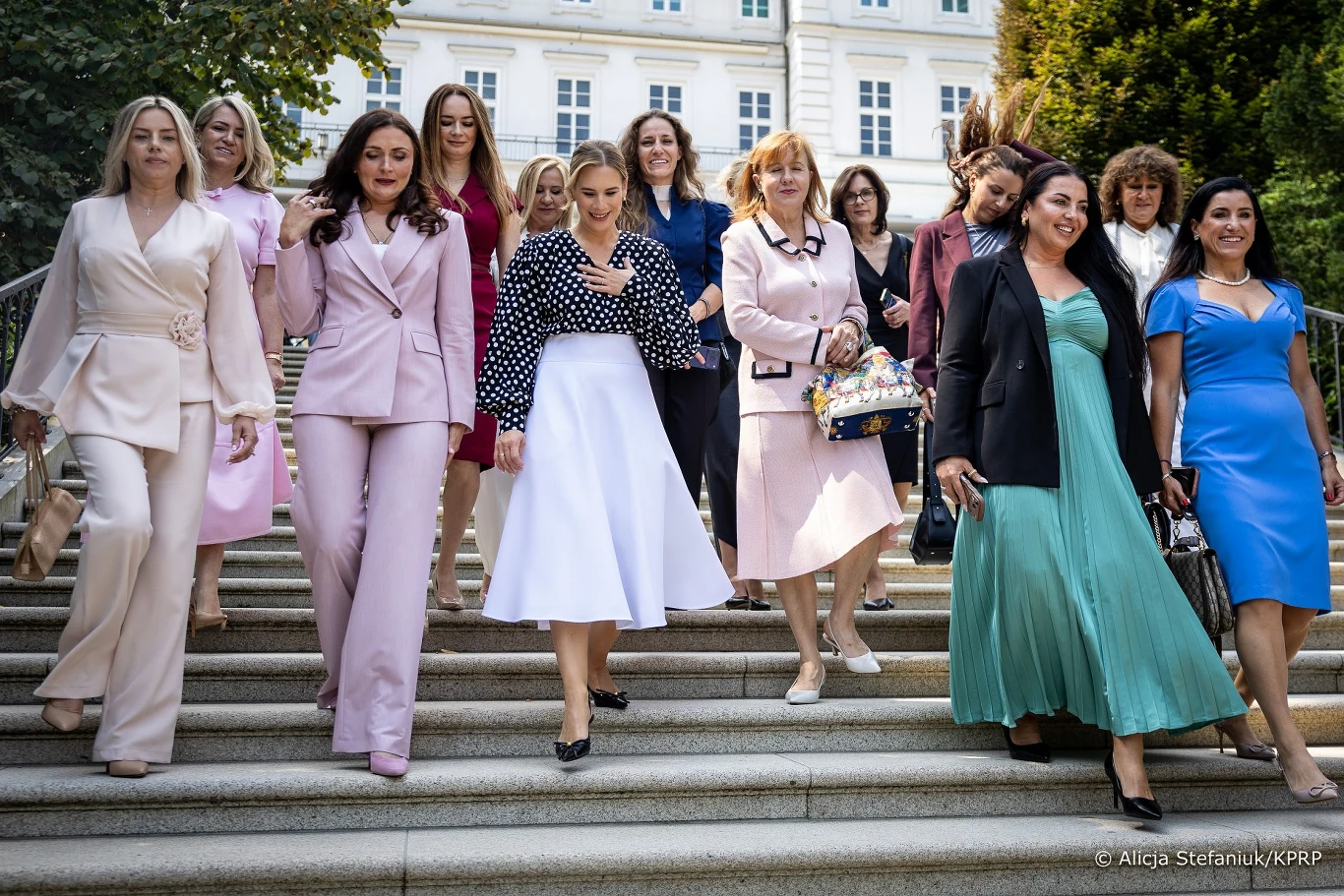 Marta Nawrocka z przedstawicielkami amerykańskiej Polonii Grupa elegancko ubranych kobiet schodzi po schodach na zewnątrz budynku, większość z nich uśmiechnięta i zaangażowana w rozmowy.
