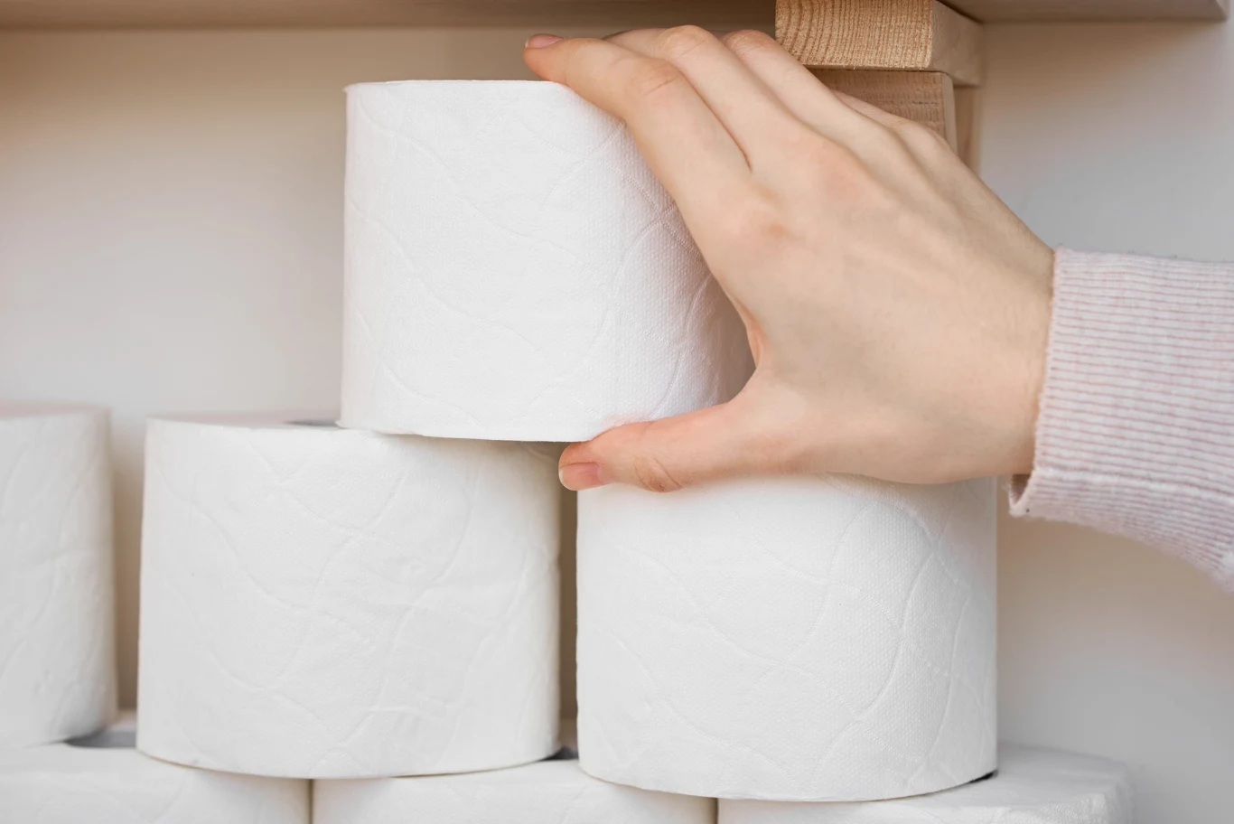 Papier toaletowy może okazać się pomocny w walce z komarami Stos białych rolek papieru toaletowego na półce, jedna rolka trzymana przez osobę w jasnej bluzce.