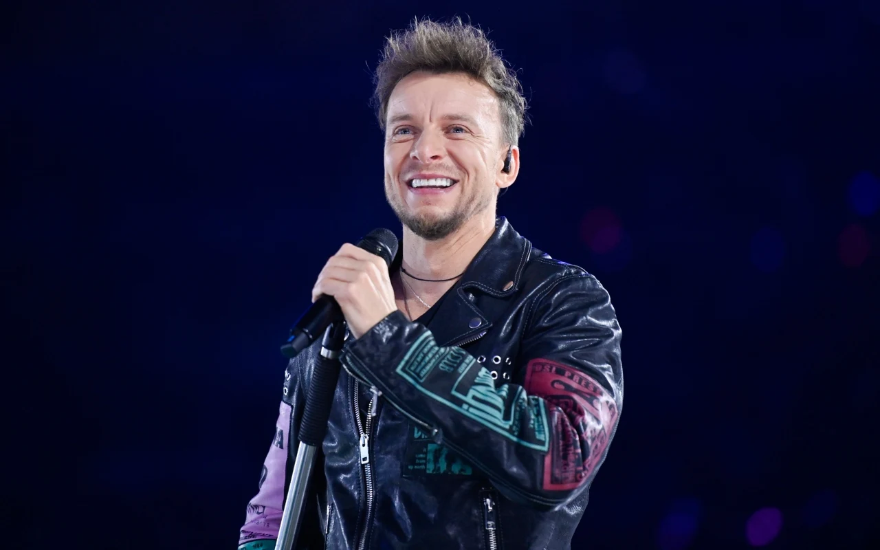 "Jak anioła głos" znała cała Polska. Piotr Kupicha zdradził, co kryło się za słowami wielkiego hitu Feel Piotr Kupicha w kolorowej kurtce trzyma mikrofon na scenie podczas koncertu zespołu Feel.