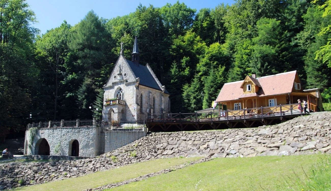 Pustelnia św. Jana z Dukli "Na Puszczy", na wzgórzu Zaśpit. Kamienny kościółek Pustelni św. Jana z Dukli i drewniany dom pielgrzyma na tle lasu, wzgórze Zaśpit.