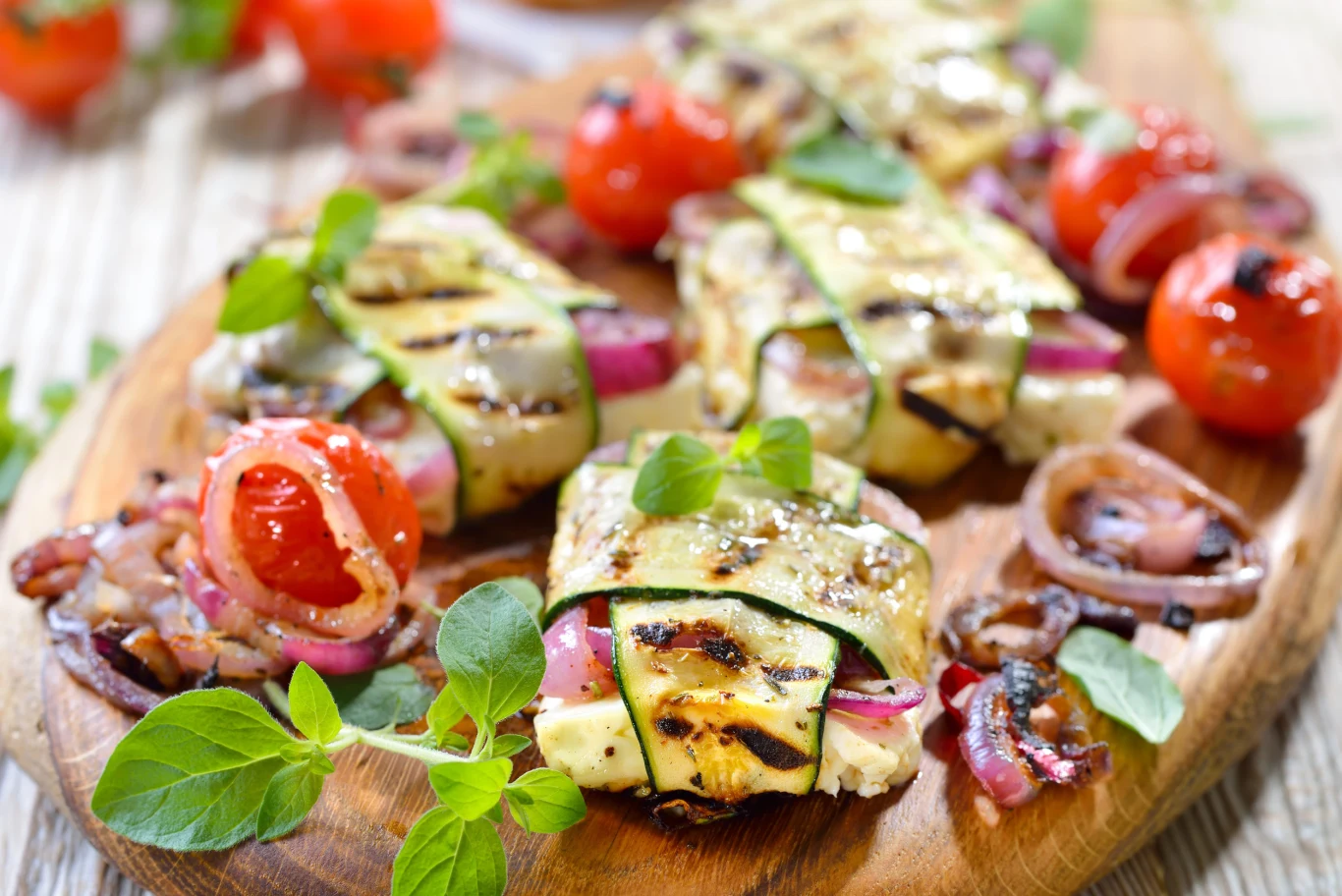 Grillowana feta z plastrami cukinii to pomysłowa przystawka na lato Grillowane roladki z cukinii z fetą i czerwoną cebulą, udekorowane ziołami, podane z pomidorkami koktajlowymi.