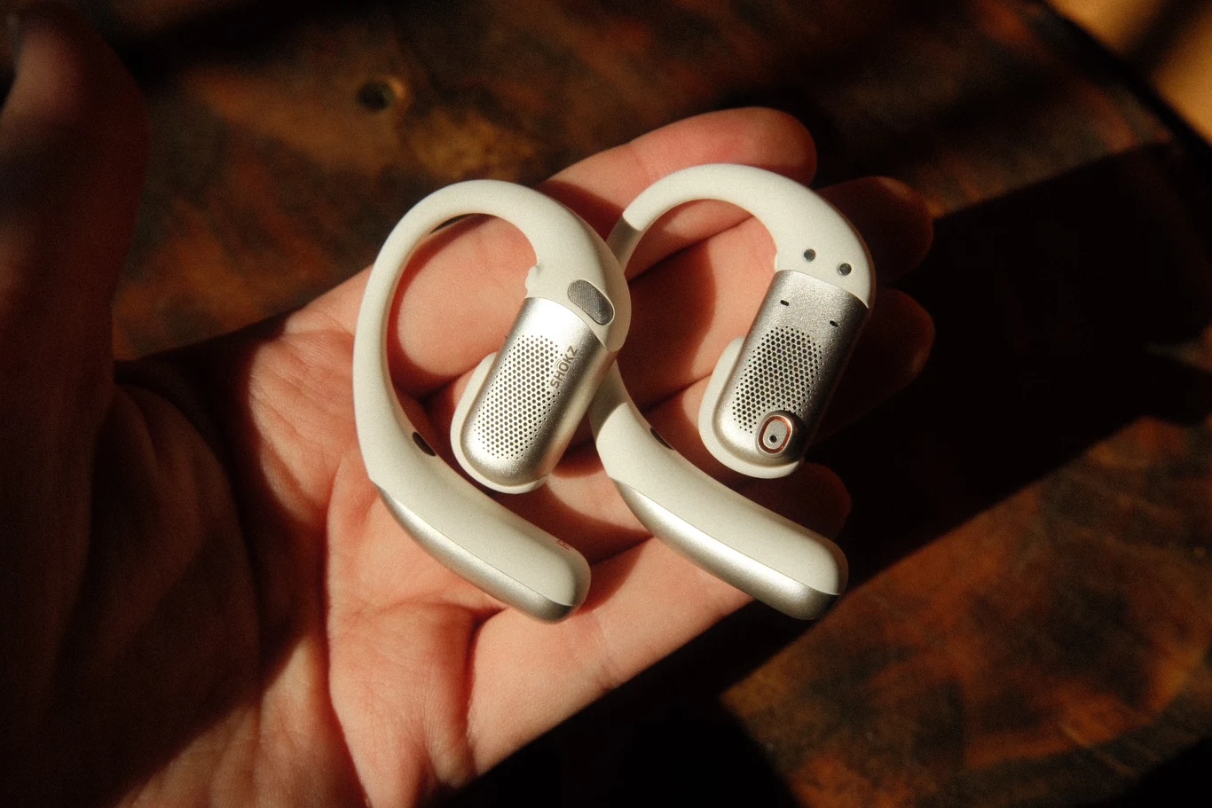 Shokz OpenFit Pro Dwie białe bezprzewodowe słuchawki douszne z zaczepami na uszy umieszczone na otwartej dłoni.