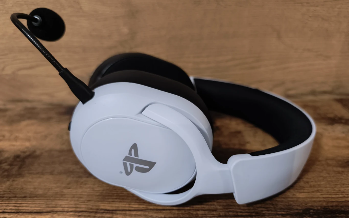 Białe słuchawki gamingowe z mikrofonem i logo PlayStation na muszli, ułożone na drewnianej powierzchni.