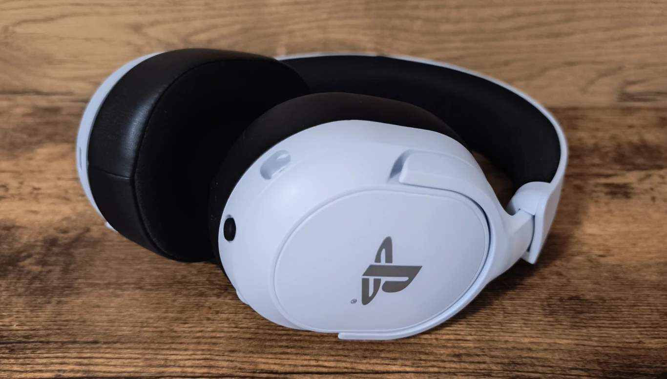 Białe bezprzewodowe słuchawki nauszne z logo PlayStation, wykonane z matowego plastiku i czarnych, miękkich poduszek nausznych, umieszczone na drewnianej powierzchni.