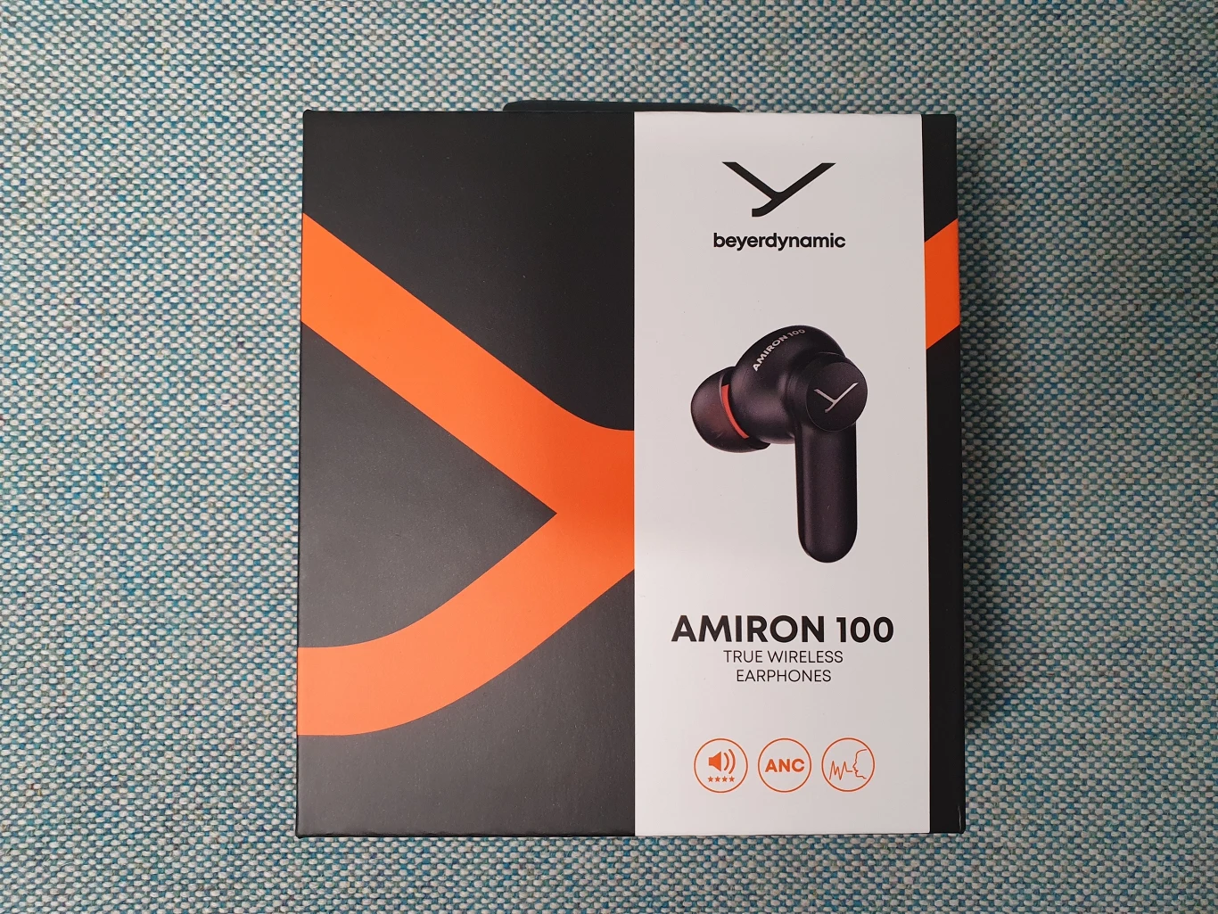 Czarno-pomarańczowe opakowanie słuchawek bezprzewodowych beyerdynamic Amiron 100 z wyeksponowanym zdjęciem jednej słuchawki oraz ikonami funkcji na froncie.