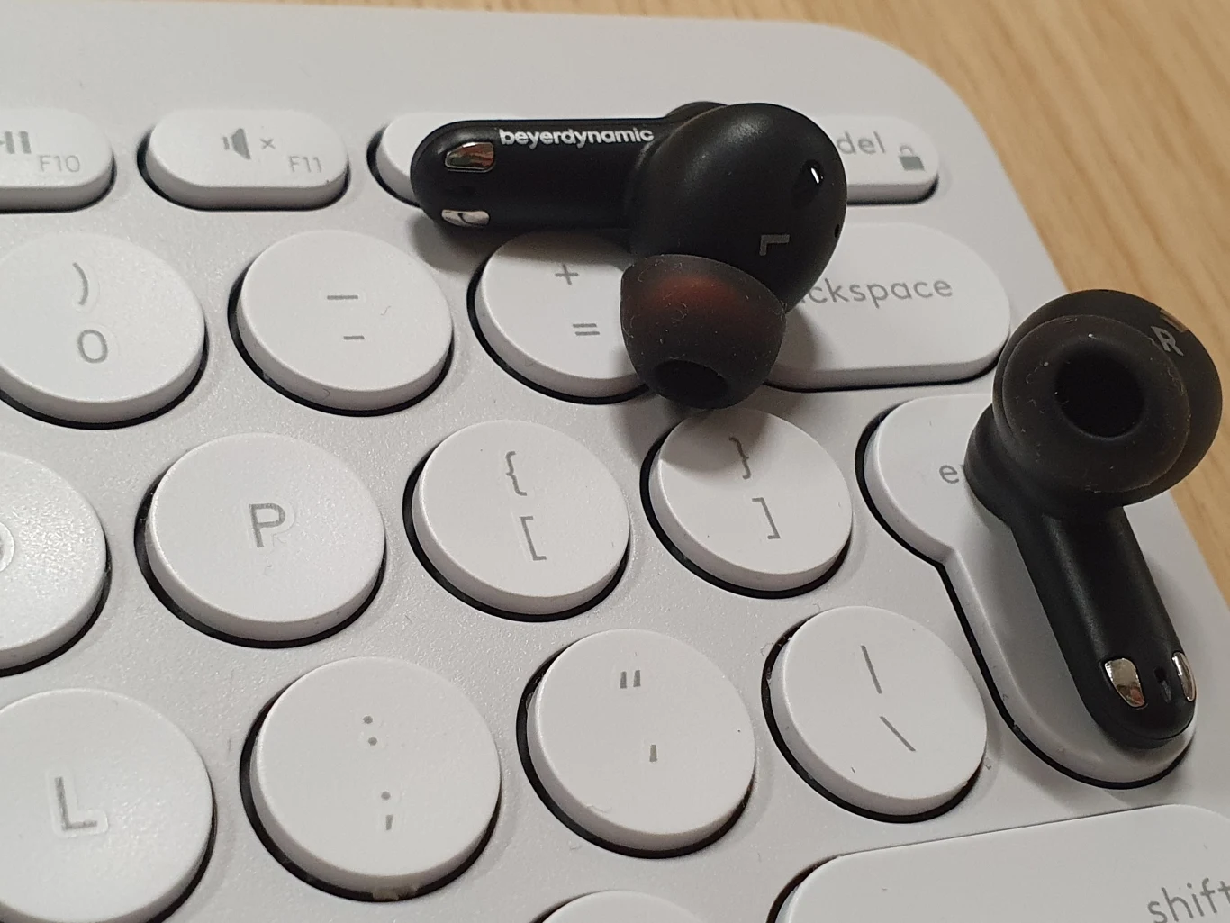 Czarne bezprzewodowe słuchawki dokanałowe marki Beyerdynamic leżące na białej klawiaturze komputerowej.