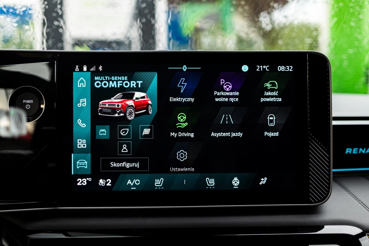 Centralny ekran systemu multimedialnego samochodu Renault z wyświetlonymi ikonami trybu jazdy, klimatyzacji, nawigacji i ustawień komfortu oraz graficzną prezentacją pojazdu.