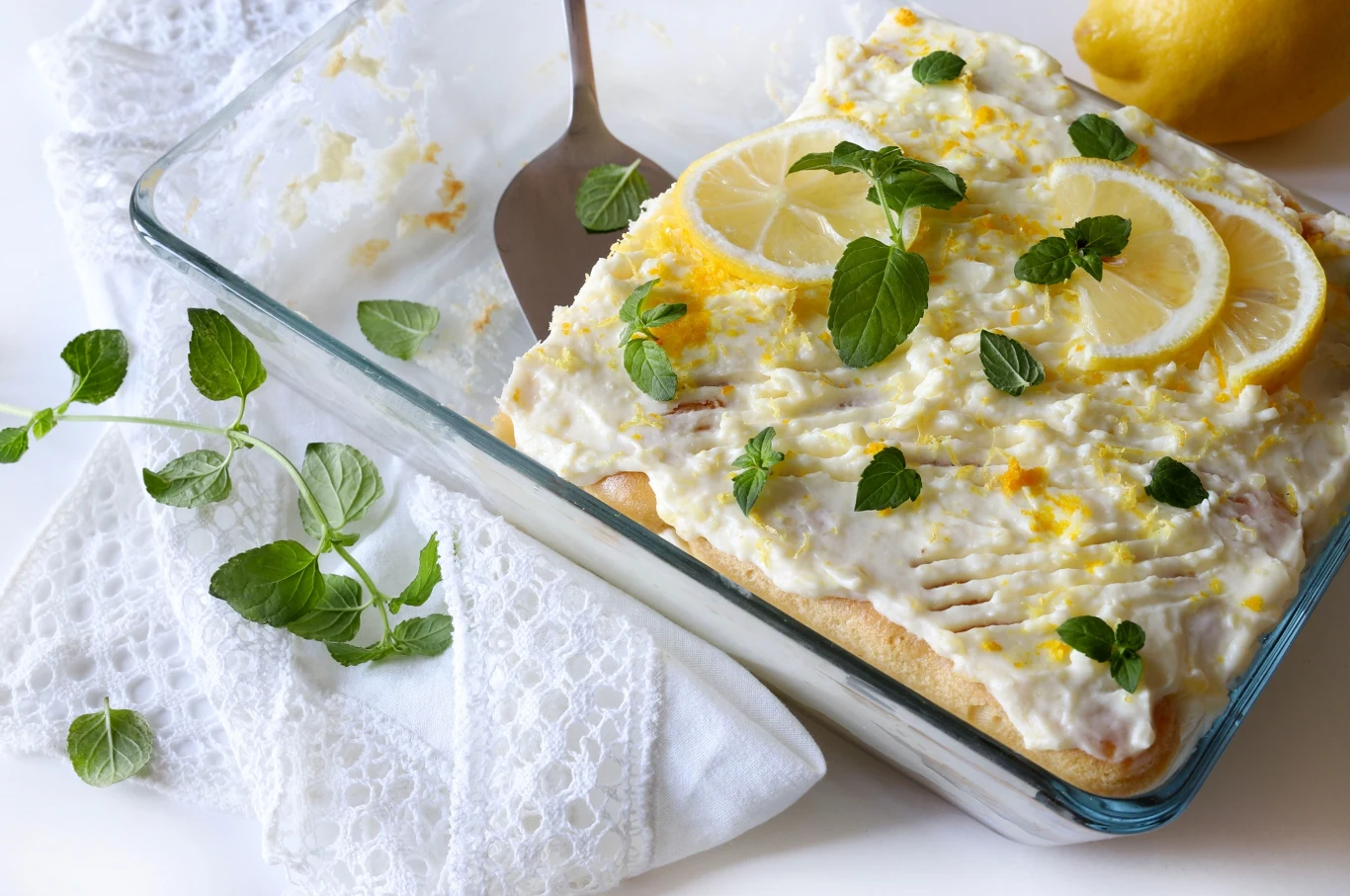 Cytrynowe tiramisu to lekka i orzeźwiająca wersja klasycznego deseru. Świetnie sprawdza się podczas upałów. Cytrynowe tiramisu w szklanym naczyniu ozdobione cytryną, skórką z cytryny i miętą.