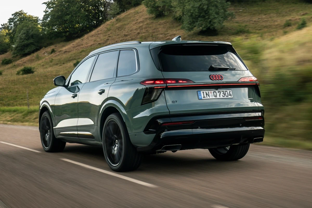 Nowoczesny SUV Audi Q7 w zielonym kolorze, jadący po asfaltowej drodze, dynamiczna sylwetka podkreślona ciemnymi felgami oraz charakterystycznym oświetleniem LED z tyłu.
