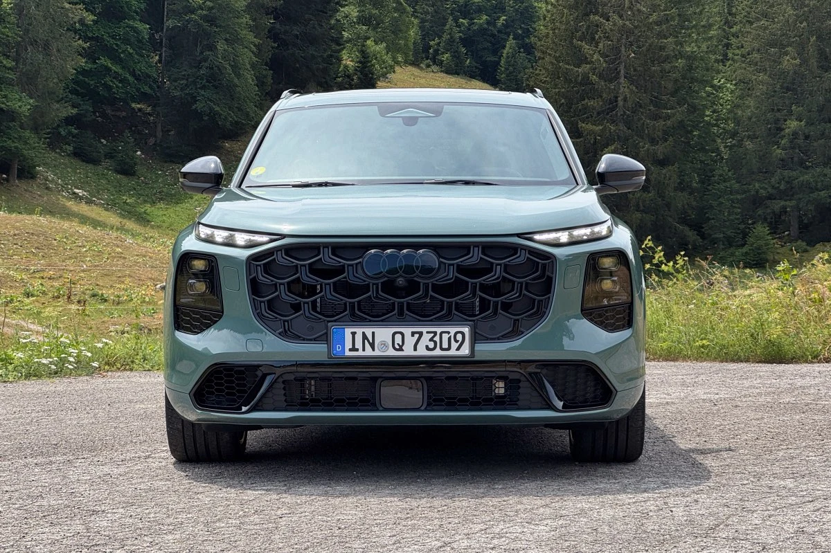 Nowoczesny SUV marki Audi z dużym, sześciokątnym grillem oraz charakterystycznymi reflektorami LED, ustawiony na tle górskiego krajobrazu i lasu.