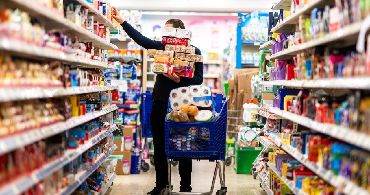 Zakupy przed długim weekendem 15–16 sierpnia 2026, co musisz wiedzieć o zamknięciu sklepów Osoba z pełnym koszykiem zakupów wybiera produkty spożywcze w alei supermarketu przed długim weekendem.