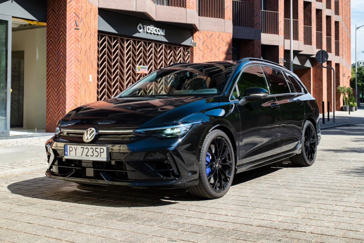 Volkswagen Golf R Czarny Volkswagen Golf Variant zaparkowany na brukowanej ulicy obok nowoczesnego budynku z czerwonej cegły.