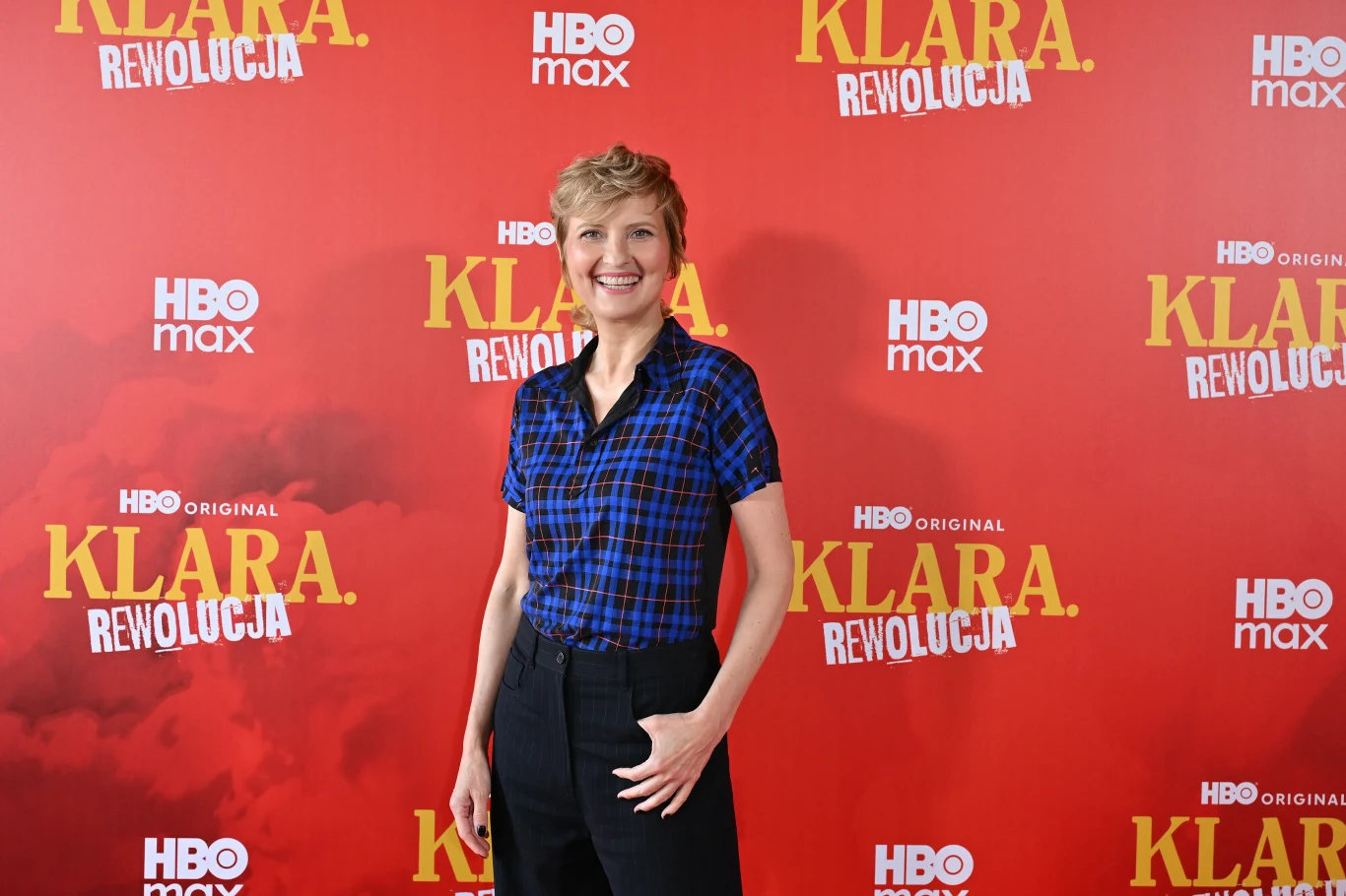 Izabela Kuna na dniu prasowym 2. sezonu serialu "Klara" Izabela Kuna na dniu prasowym 2. sezonu "Klara", w koszuli w niebieską kratę i czarnych spodniach na tle ścianki.