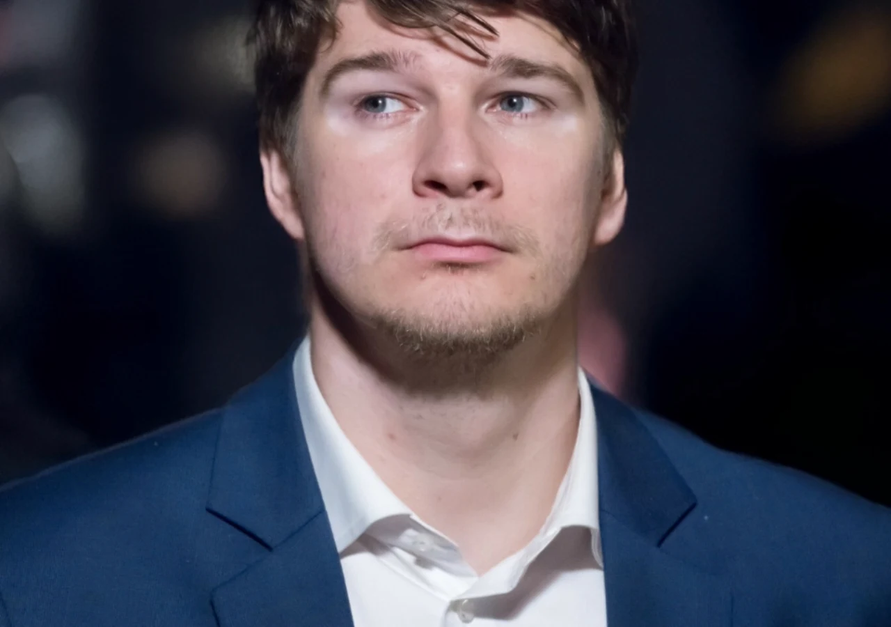 Mężczyzna w granatowej marynarce i białej koszuli spoglądający w bok z poważnym wyrazem twarzy.